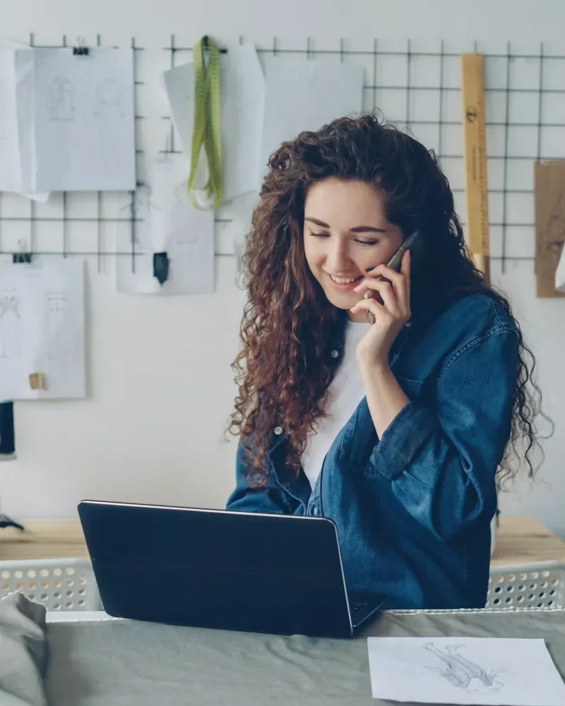 Freelance fashion designer on a phone call while working on her laptop